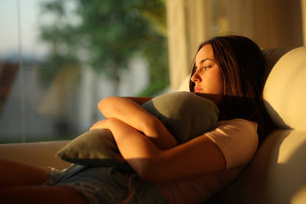Isolated woman at sunset at home complaining hugging pillow