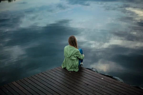 A girl in depression was sitting alone in front of sky .
