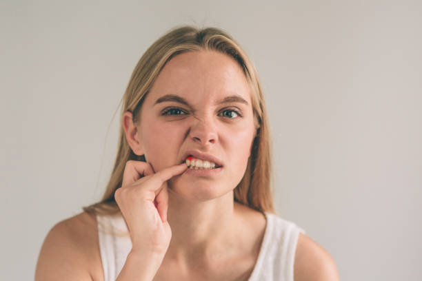 A horizontal photo of a young worried woman in checkered shirt suffering from gum diseases and touching her cheek.