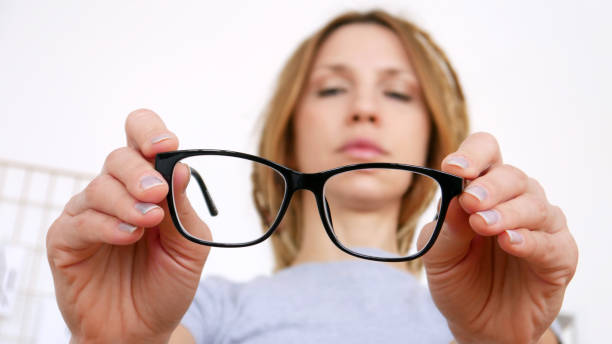A young woman with myopia holding black-framed glasses in her hands inspecting them