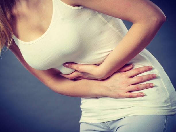 Health care concept. Bellyache, indigestion or menstruation. Young female suffering from strong PCOS pain on gray
